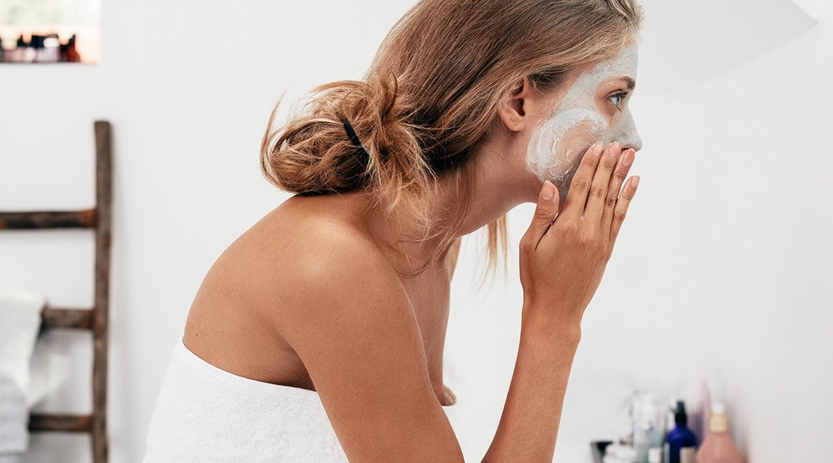 Eine Frau traegt sich eine Gesichtsmaske auf